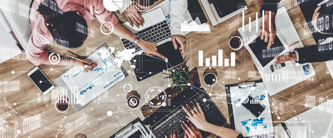 foto de varias maos em uma mesa, segurando notebooks, tablets, papeis com dados e cafés